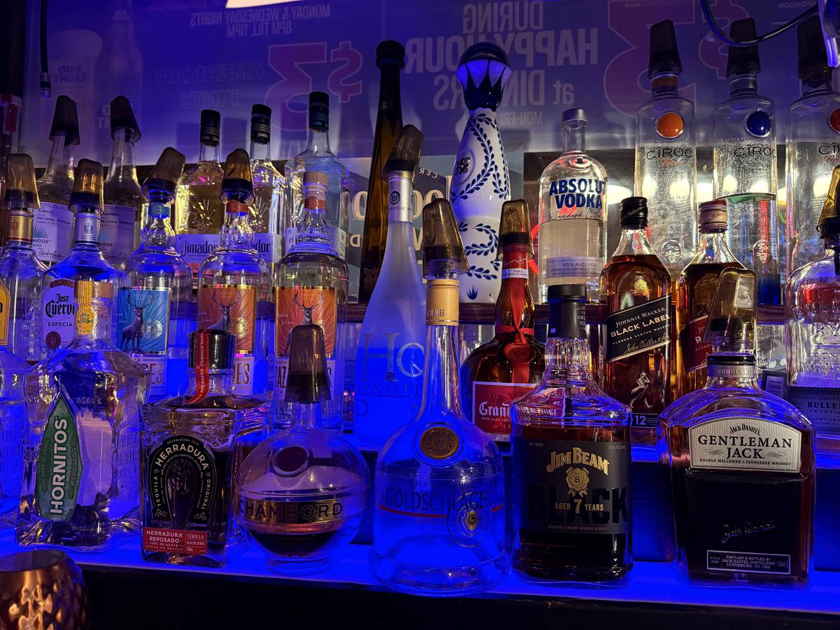 Back bar at Dingers Sports Bar, second angle. More bottles readable under cobalt LED lighting. Same electric blue color cast.