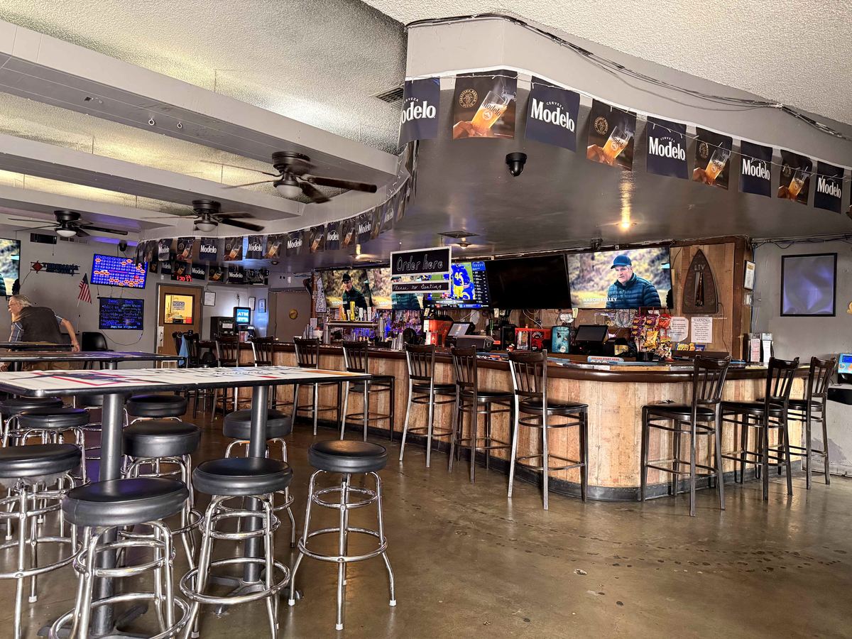 The main room at Dingers Sports Bar and Grill in San Bernardino. Bar stools, high-tops, Modelo banners, TVs on. The kitchen opens at 8 PM every night.
