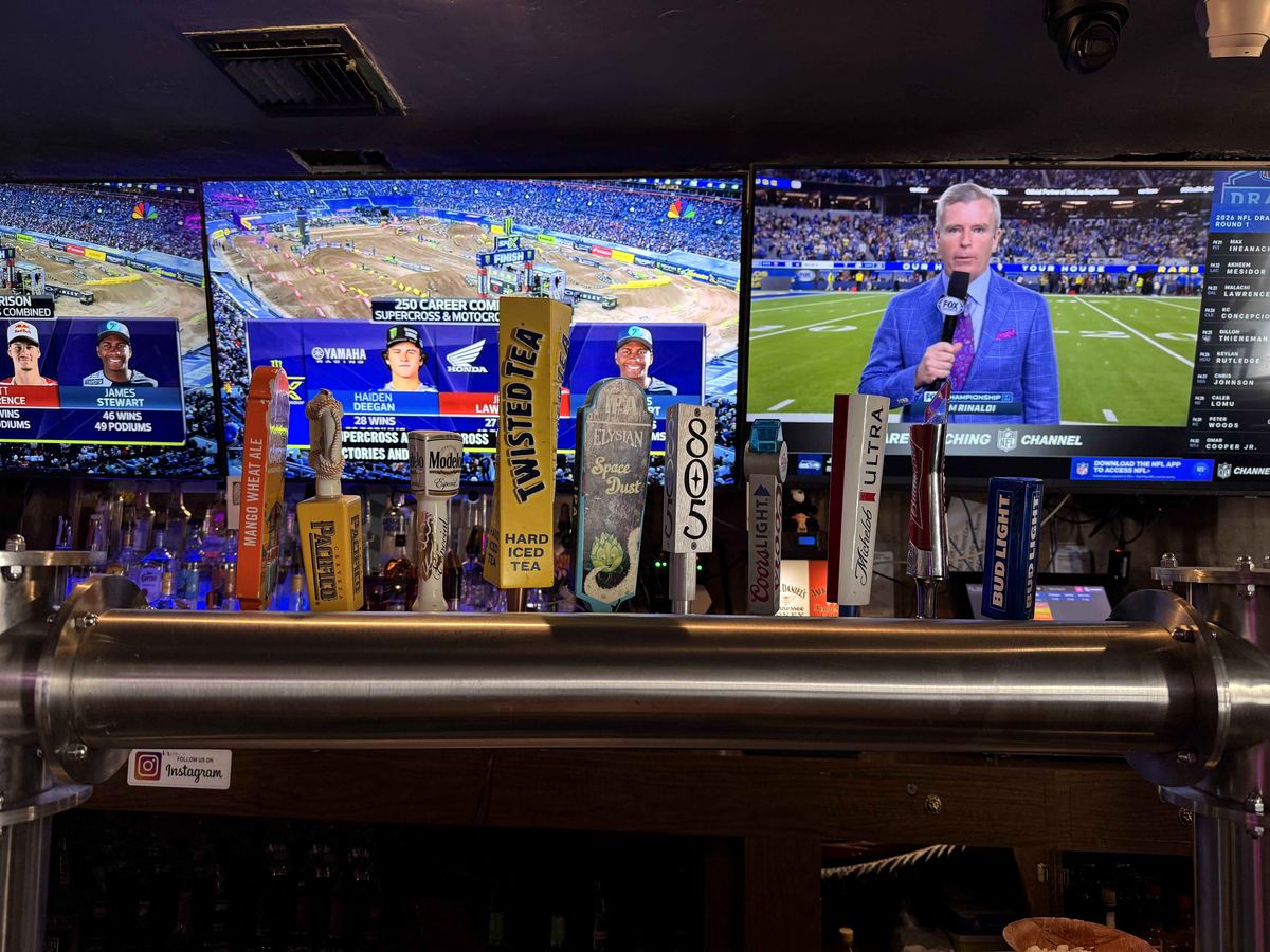 Tap handles at Dingers Sports Bar showing Twisted Tea, 805, Modelo, Michelob Ultra, Bud Light. Two large TVs visible in the background showing different sports broadcasts.