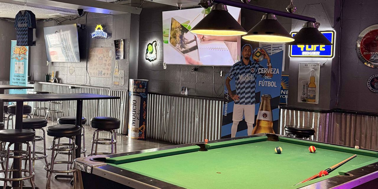 A pool table under a three-lamp light at Dingers Sports Bar, with high-top tables, a Modelo cutout, and beer signs on the back wall.
